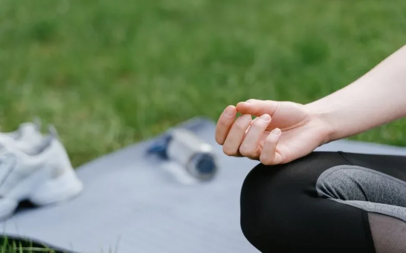 Close-up of a woman meditating outdoors on a mat. Focus on tranquility and mindfulness.