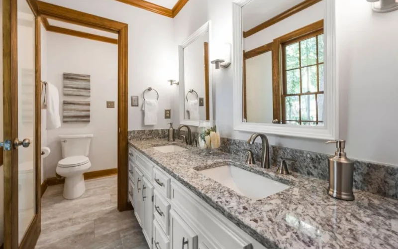 A stylish bathroom interior featuring dual sinks, granite countertops, and wooden accents. Modern and fresh design.