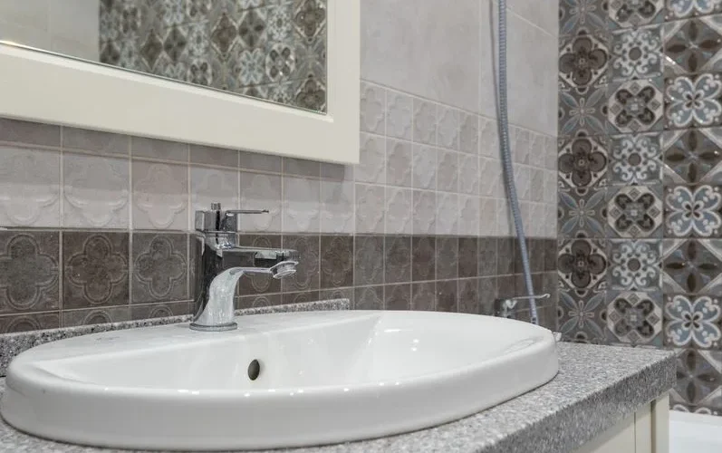 Close-up of a modern white sink and faucet with ornate patterned tiles in the bathroom.