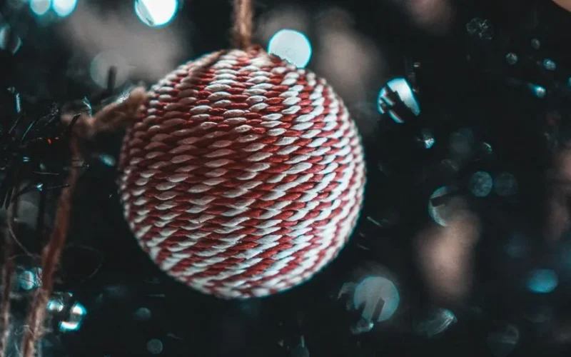 Close-up of a woven Christmas bauble hanging on a tree with bokeh effect.