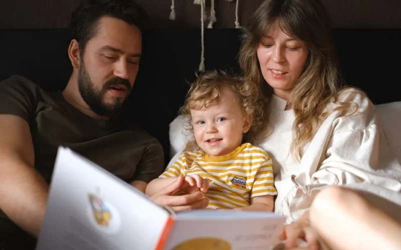 A happy family reading together, featuring parents and their smiling child enjoying a book indoors.