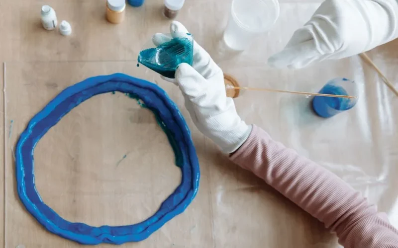 Close-up of hands crafting blue resin art indoors, showcasing artistic process.