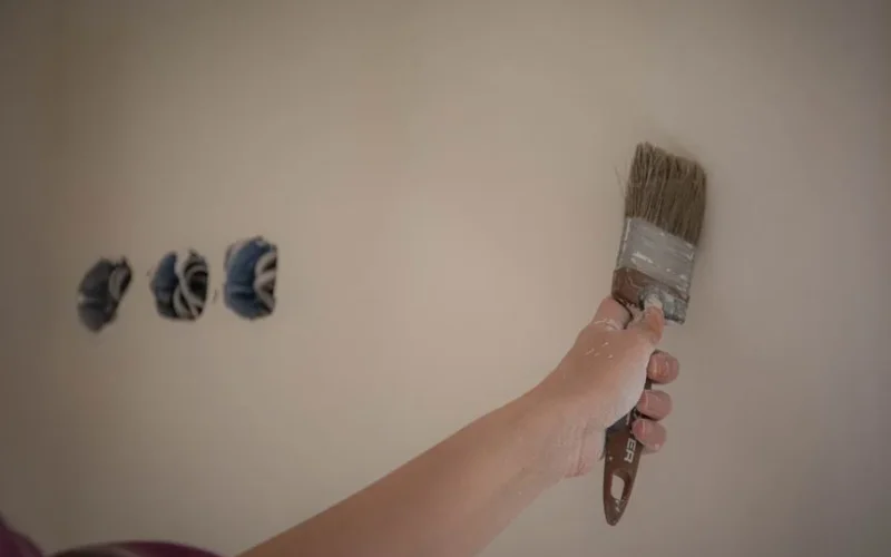 A person painting a wall with a brush, showcasing a home makeover process.