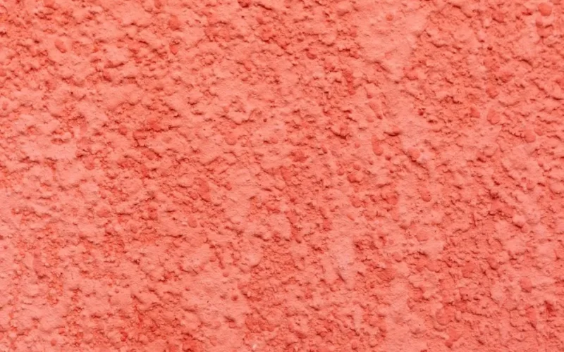 Textured surface of bright wall covered with decorative stucco of bright coral color