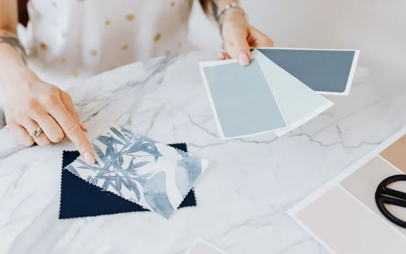 Woman selecting color and fabric swatches on marble desk for interior design project.