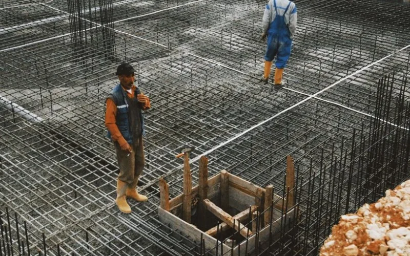 Workers preparing steel reinforcement at a construction site for concrete foundation.