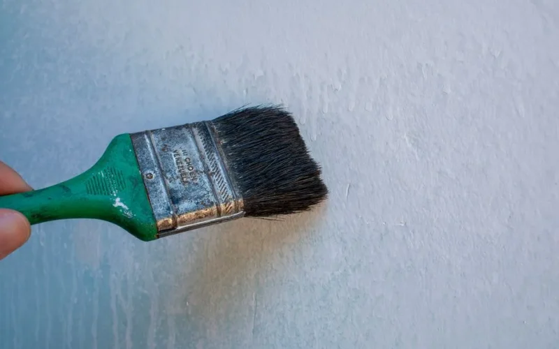 Close-up of a hand painting a wall with a paintbrush, perfect for renovation and DIY themes.