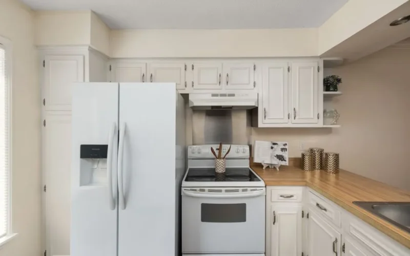 Stylish white kitchen featuring modern appliances, wooden countertop, and decorative accents.