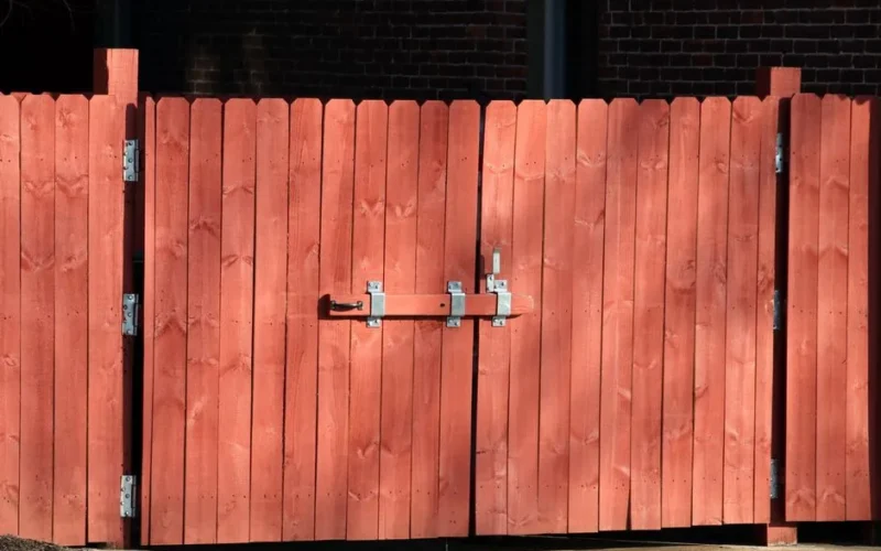 Rustic red wooden fence with a metal latch, ensuring safety and security outdoors.