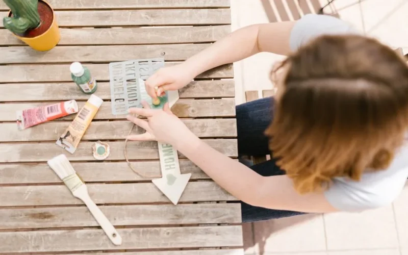 A person engaged in an outdoor crafting and painting activity on a wooden table.