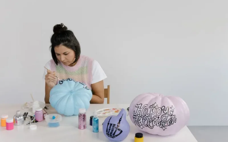 Woman painting pumpkins for Halloween with art supplies on a table.