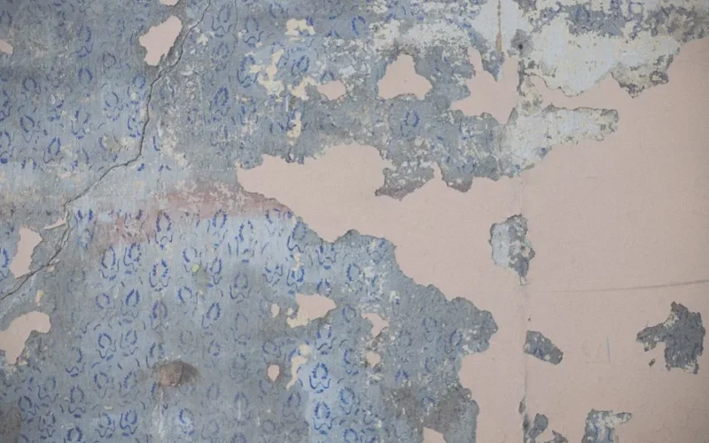 Close-up of distressed peeling wallpaper with vintage blue floral patterns creating a rough texture.