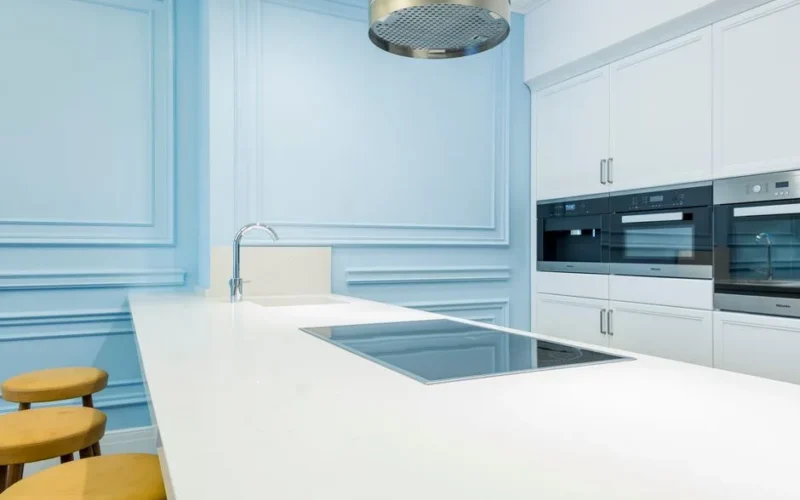 Bright, modern kitchen with minimalist design featuring blue walls and sleek white countertops.