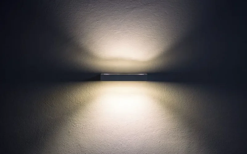 Artistic wall lamp casting soft shadows, creating a minimalist ambiance in a dim setting.