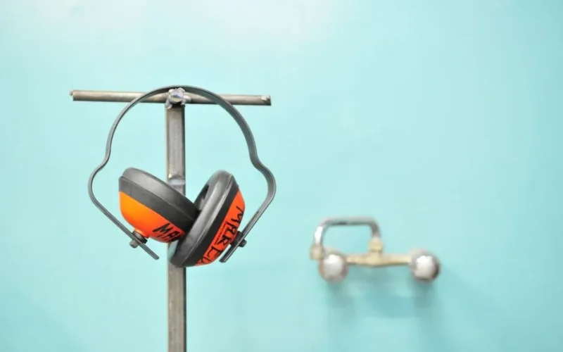 Close-up of earmuffs hanging on a metal stand in front of a teal wall.