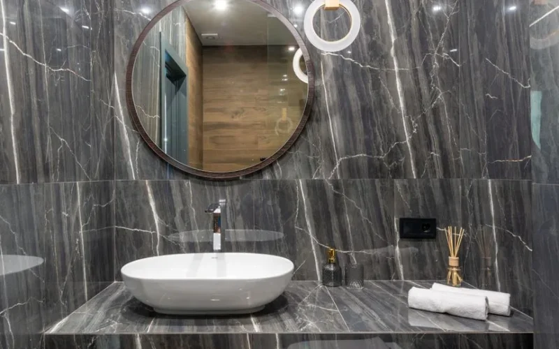 Elegant bathroom featuring a modern sink, round mirror, and marble finishes.