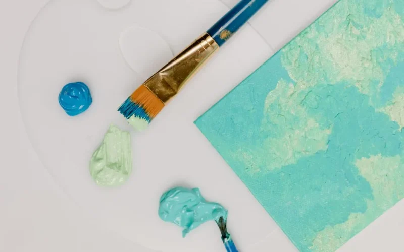 Top view of vibrant paint and brush on a white palette, showcasing artistic creativity.