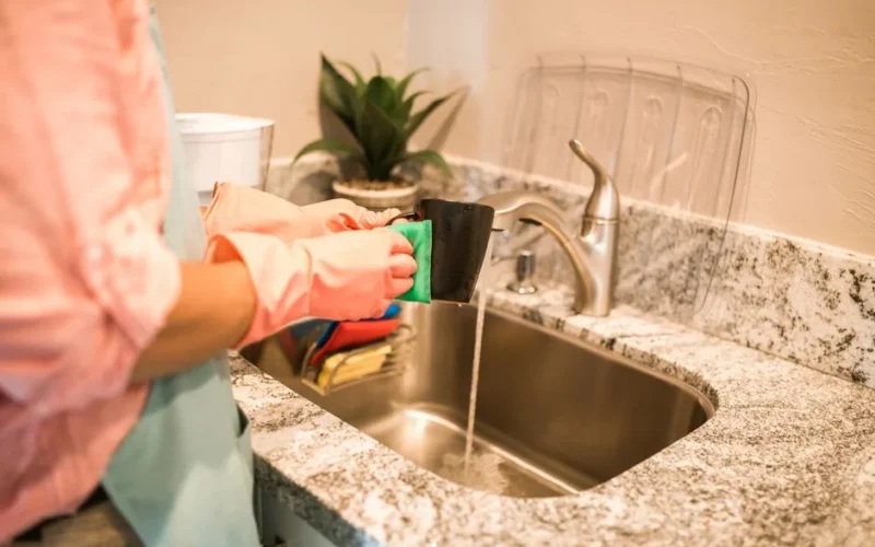 A person wearing gloves washing a mug at a kitchen sink, emphasizing cleanliness and chores.