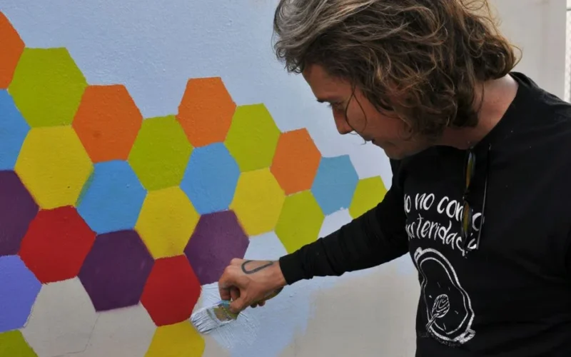 A man paints a vibrant hexagonal mural in Caguas, showcasing artistic creativity.