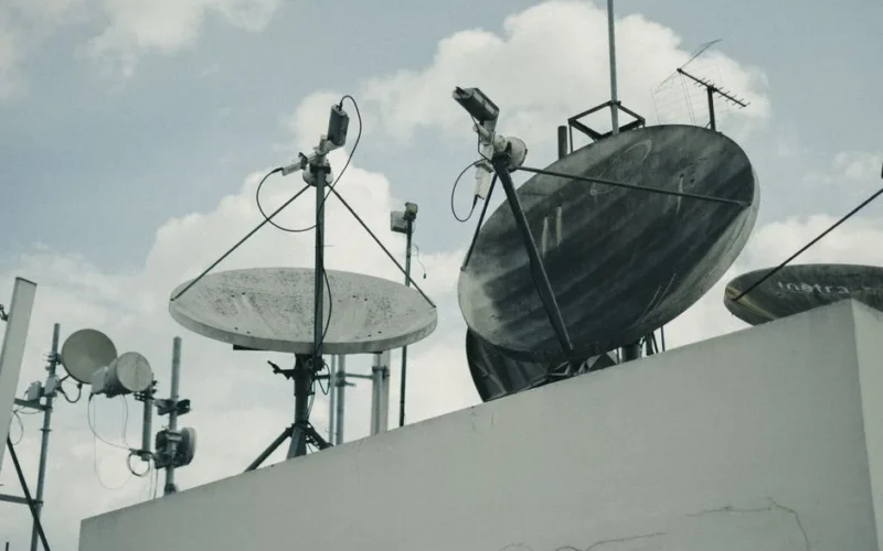 A detailed view of satellite dishes and antennas on an urban rooftop under a cloudy sky.