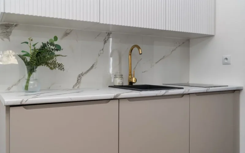 Elegant kitchen interior with marble counters and a gold faucet, featuring greenery for a touch of nature.