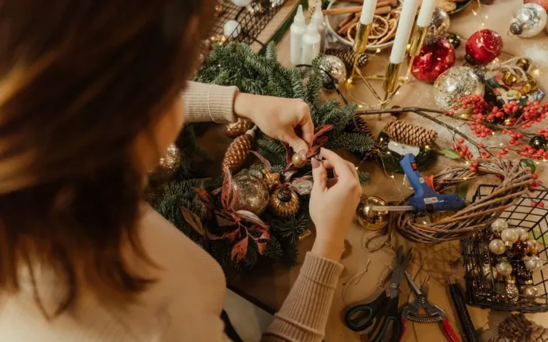 Woman arranging Christmas decorations on a wreath, crafting holiday decor.
