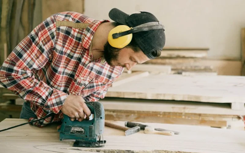 A skilled carpenter wearing protective gear works intently with a jig saw in his workshop.