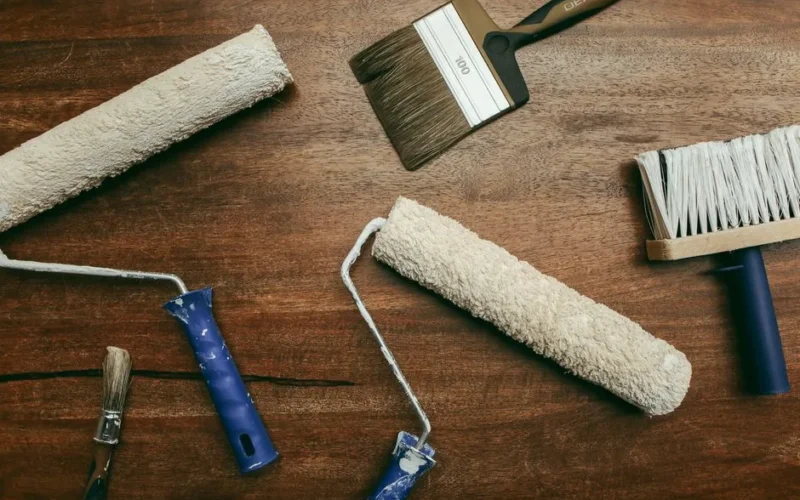 Top view of various painting tools including rollers and brushes laid out on a wooden surface.
