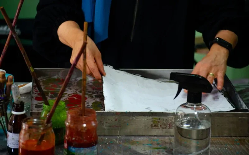 An artist's hands preparing a canvas with brushes and paints for creative work indoors.