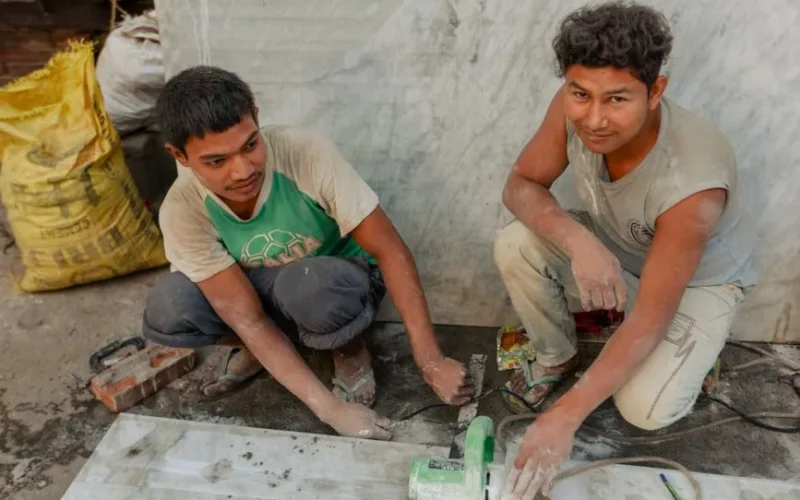 Two craftsmen using a tile cutter in a construction setting, working on a floor project.