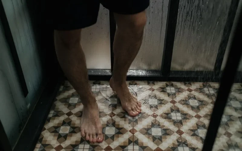 Close-up view of a person standing with wet feet on a tiled shower floor.