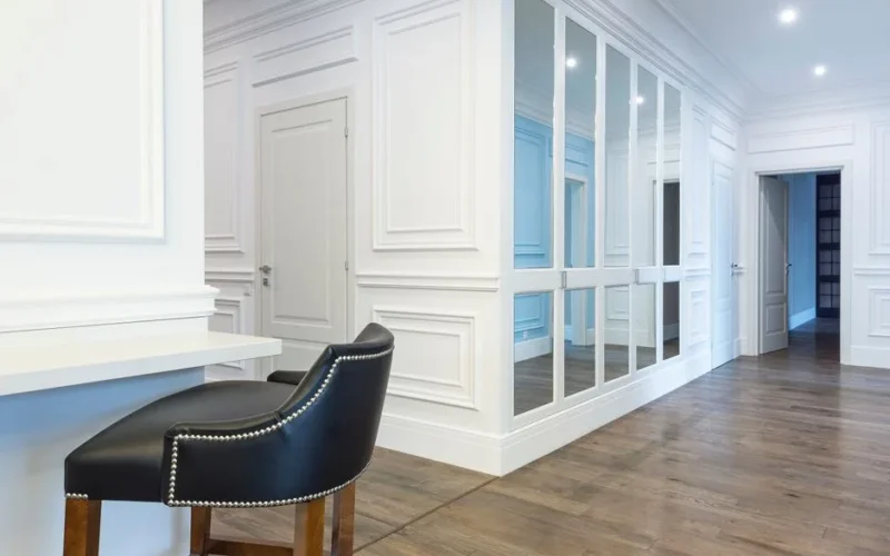 Spacious contemporary interior features white panel walls, mirrored doors, and elegant wooden flooring.