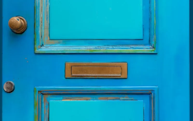 Close-up of a vintage blue wooden door featuring a brass mail slot and door knob.