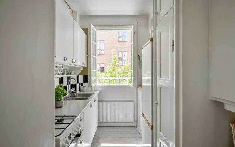 A bright and contemporary small kitchen with white cabinets and open window.
