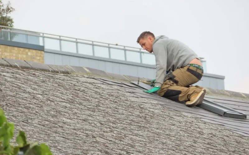 Construction worker installing shingles on a rooftop. Outdoor building maintenance.