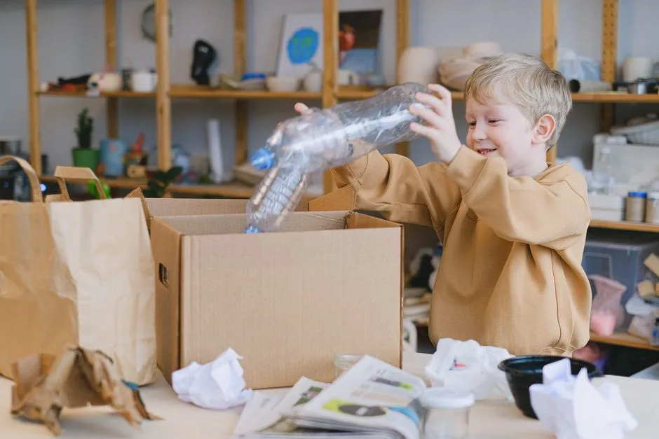 A young boy happily sorts plastic bottles into a cardboard box for recycling.