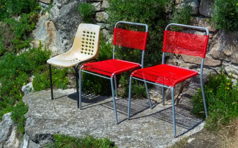 Three colorful chairs on a sunlit rocky terrace surrounded by lush greenery, offering a vibrant outdoor seating arrangement.